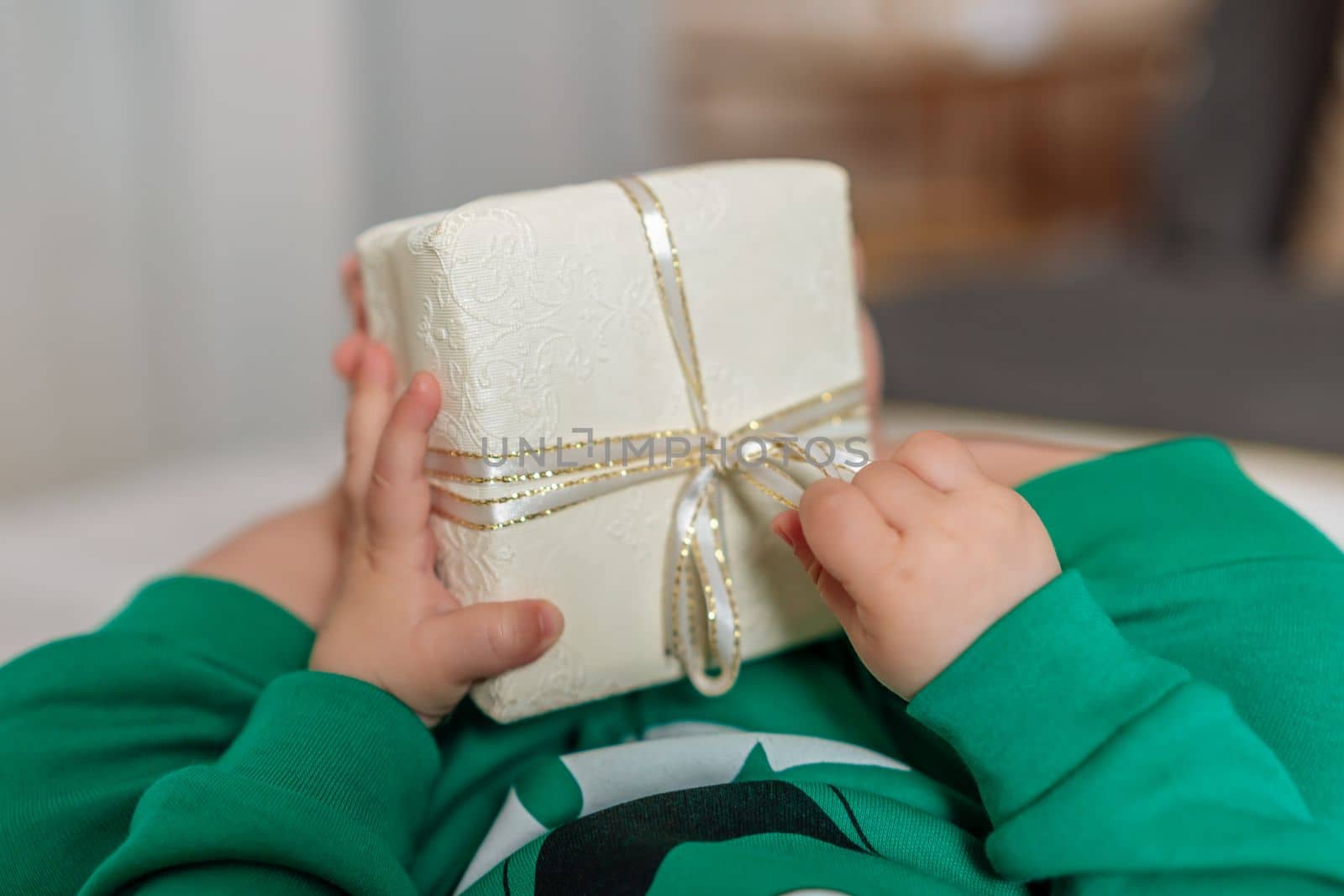 Kid gift. A little boy in a green suit holds a gift box with his feet and hands in bed