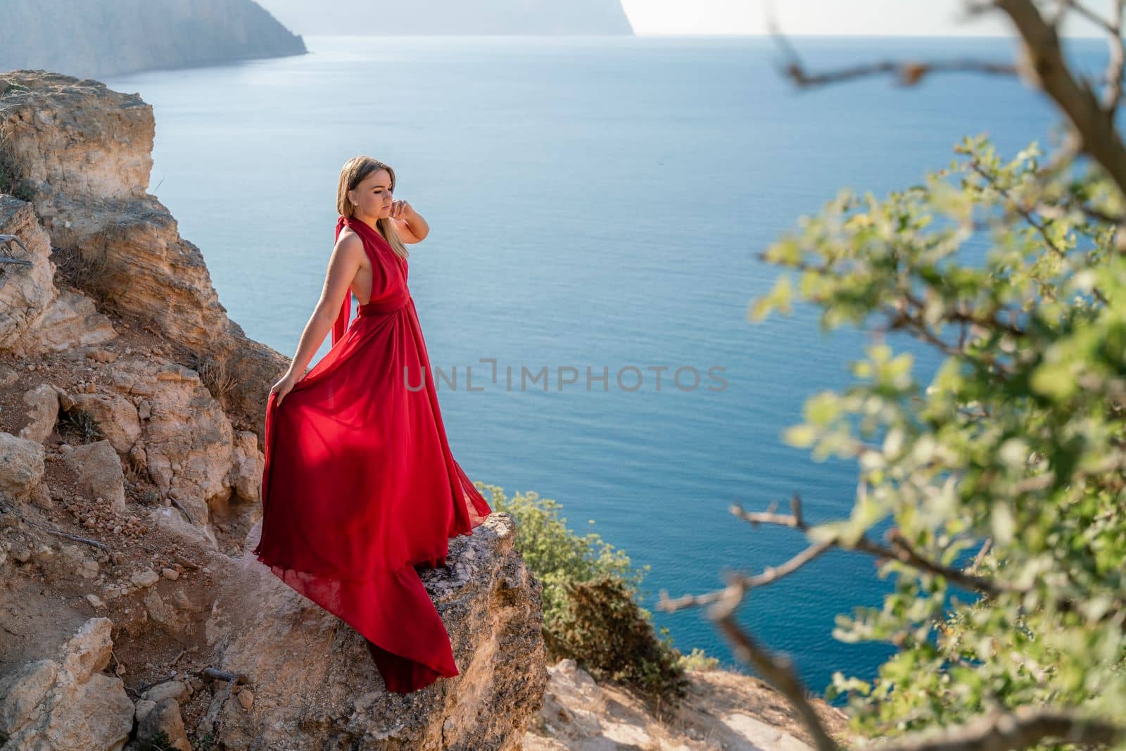 A woman in a red flying dress fluttering in the wind, against the backdrop of the sea