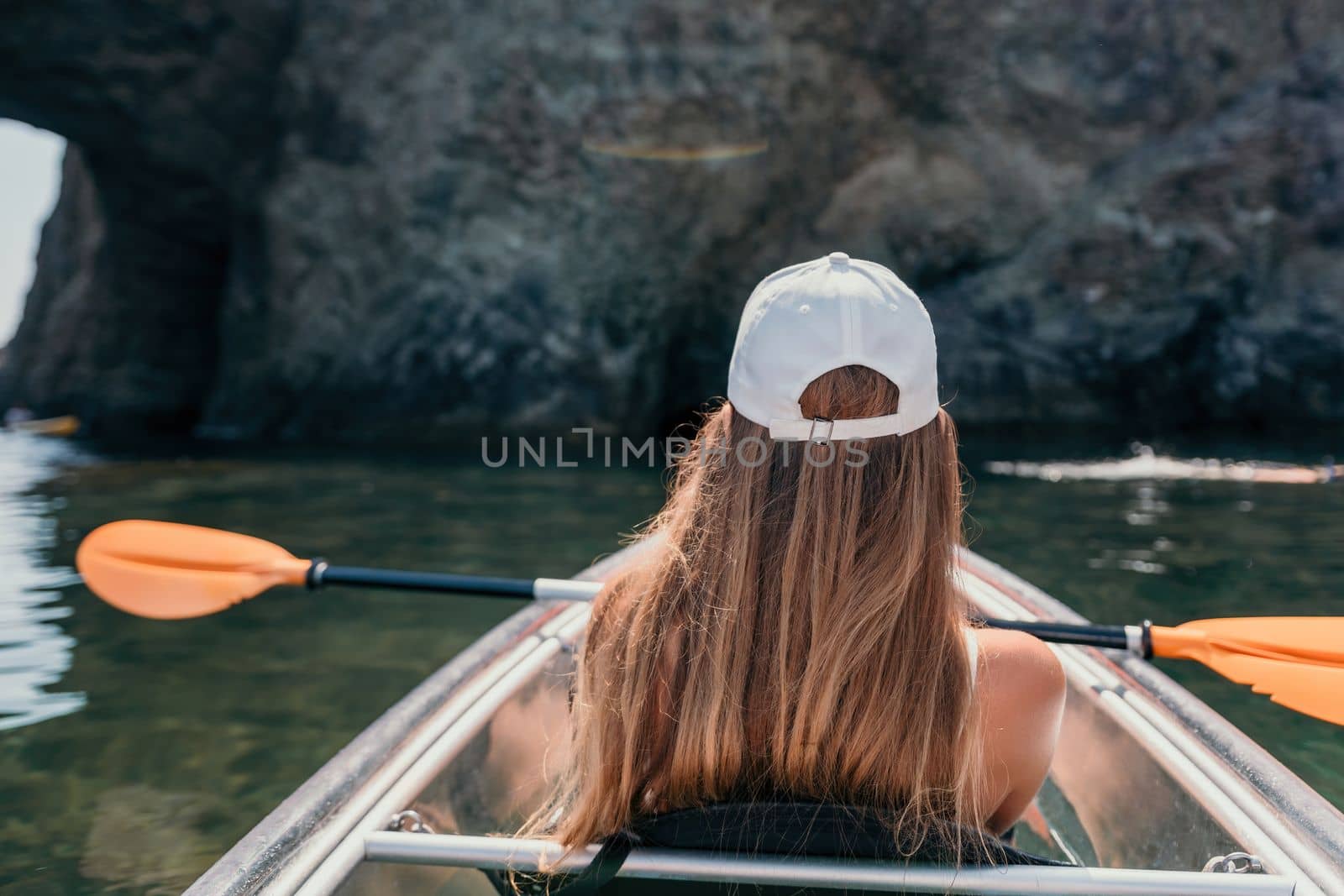 Woman in kayak back view. Happy young woman with long hair floating in transparent kayak on the crystal clear sea. Summer holiday vacation and cheerful female people having fun on the boat.