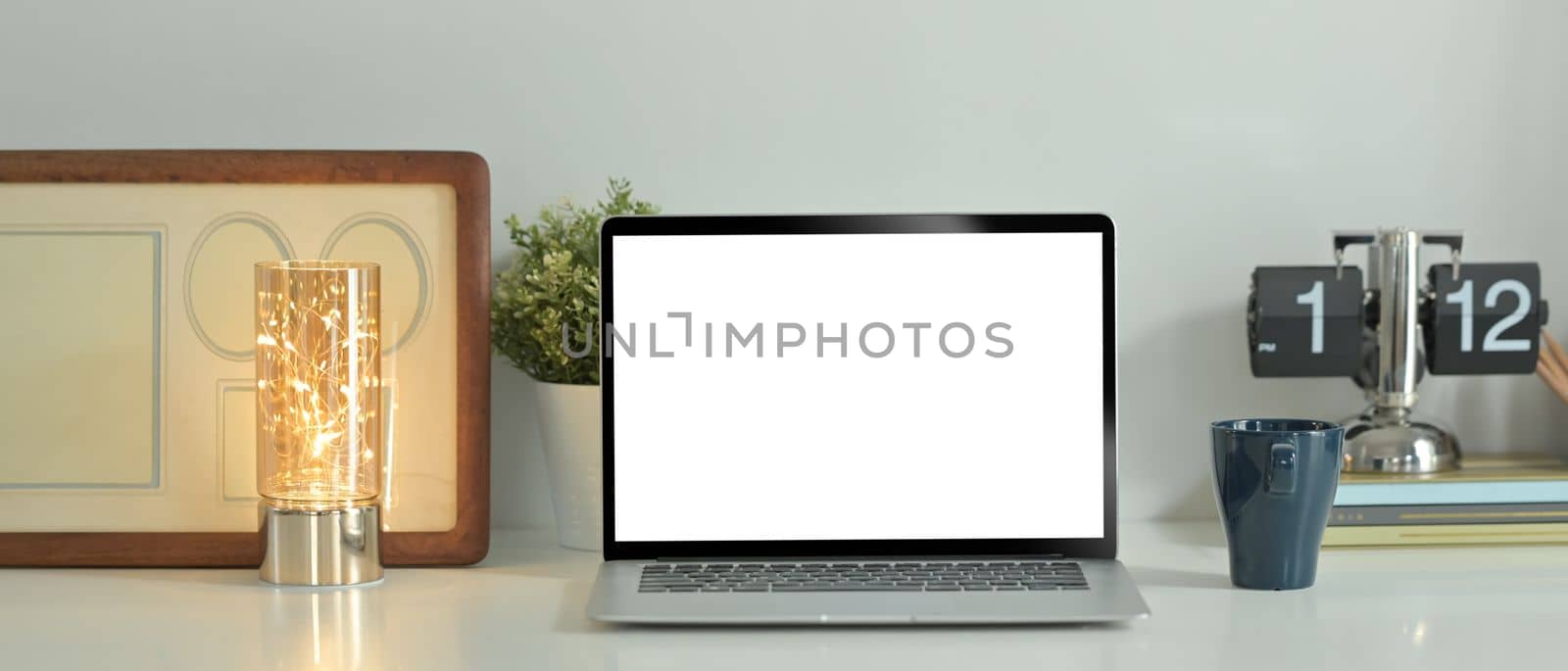 Laptop computer, coffee cup, picture frame and potted plant on white table. Blank screen for text information or content.