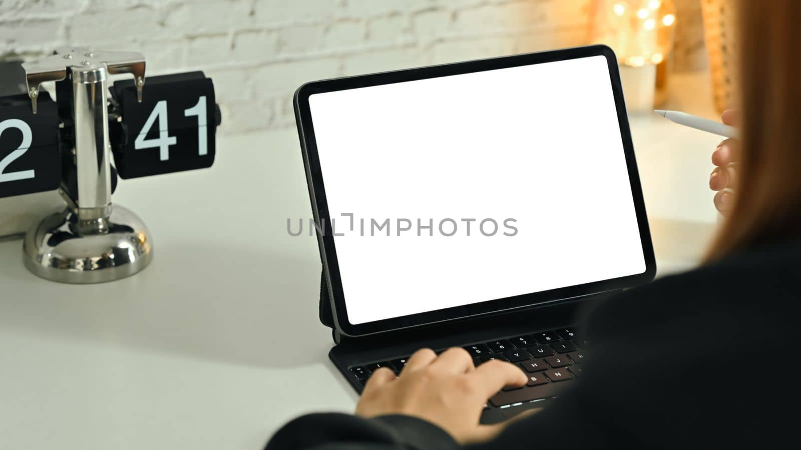 Over shoulder view of young woman using digital tablet on white working desk.