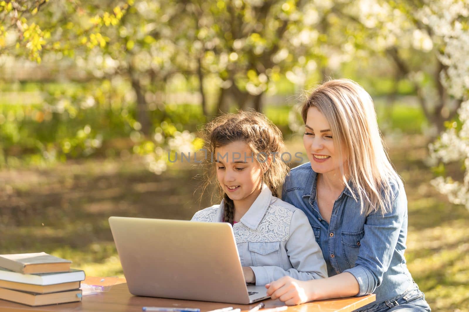 little girl with mom learning on laptop outdoor.