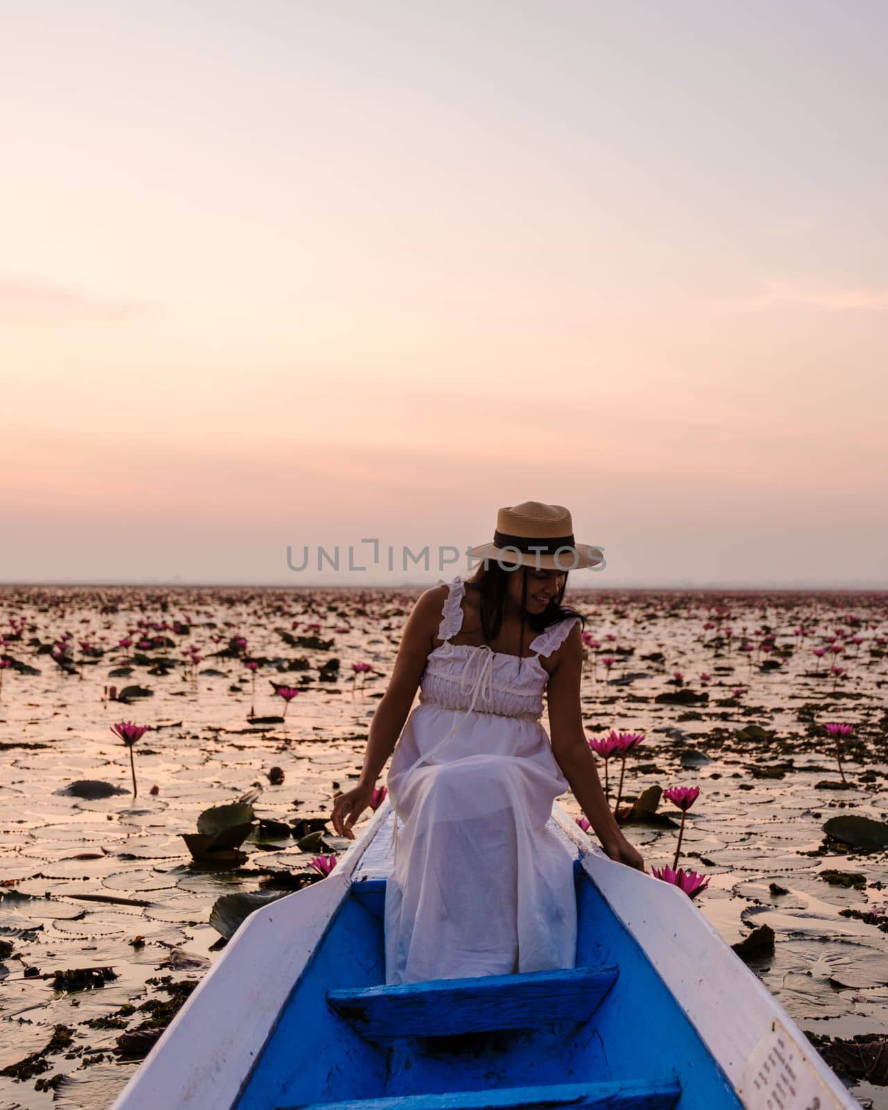 Asian women with a hat in a boat at the Red Lotus Sea full of pink flowers in Udon Thani Thailand. by fokkebok