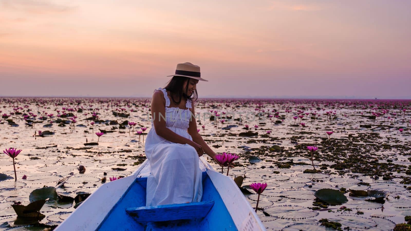 Asian women with a hat in a boat at the Red Lotus Sea full of pink flowers in Udon Thani Thailand. by fokkebok