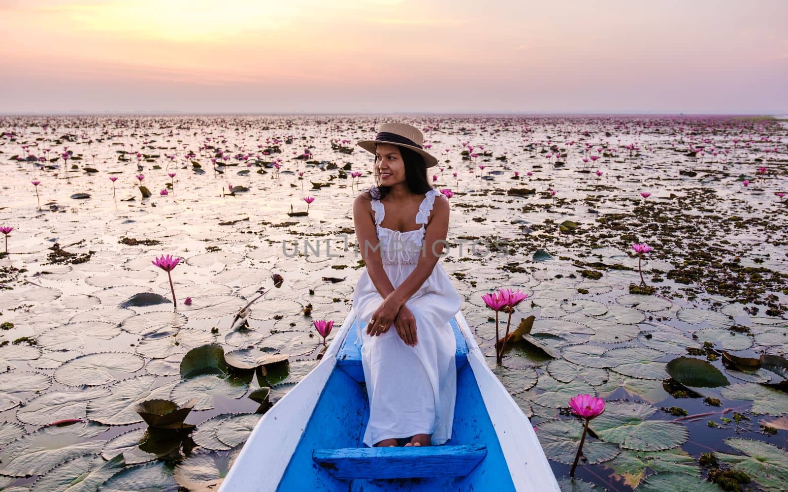 Asian women in a boat at the Beautiful Red Lotus Sea Kumphawapi is full of pink flowers in Udon Thani in northern Thailand. Flora of Southeast Asia.