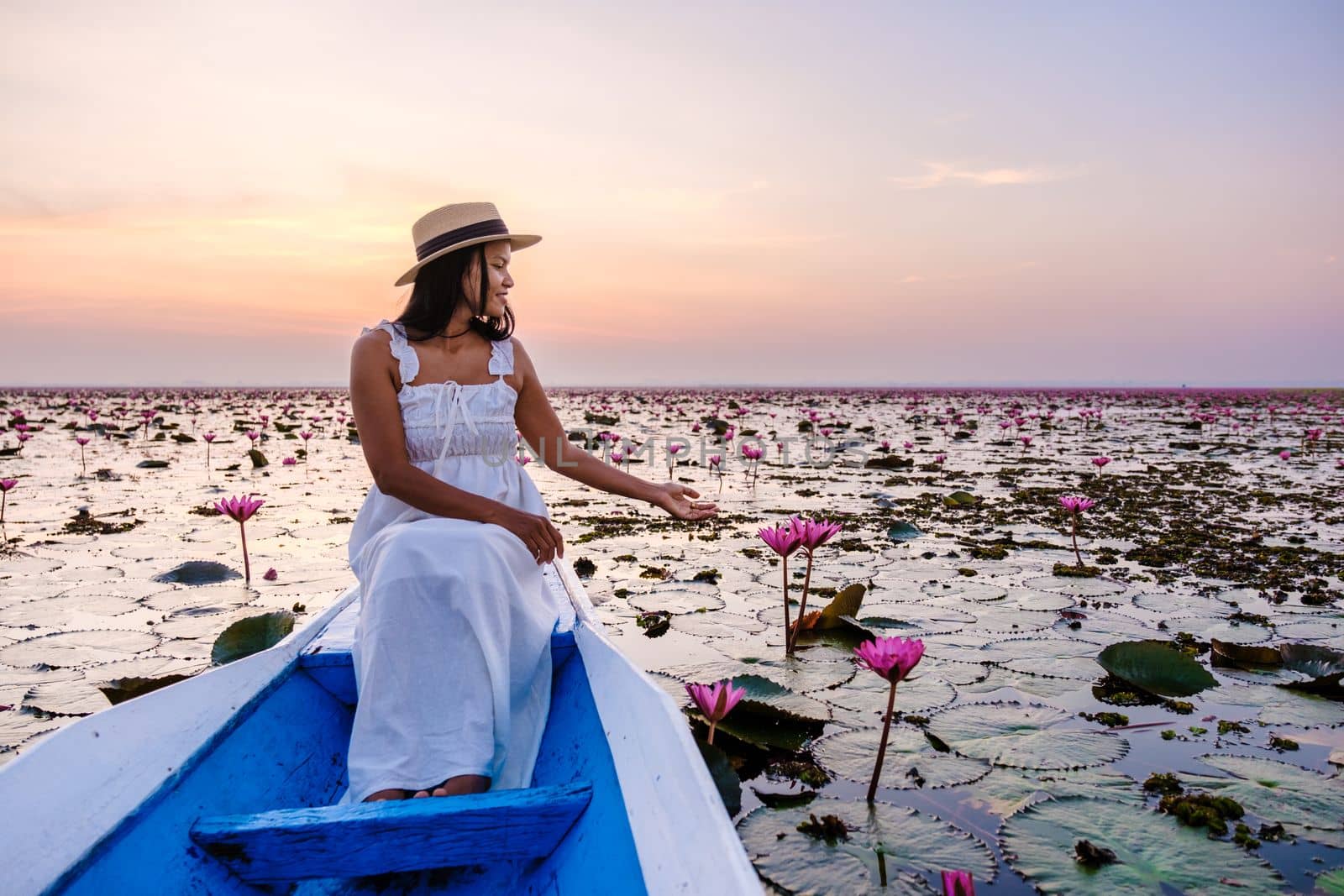 Asian women in a boat at the Beautiful Red Lotus Sea Kumphawapi is full of pink flowers in Udon Thani in Northern Thailand Isaan. Flora of Southeast Asia.