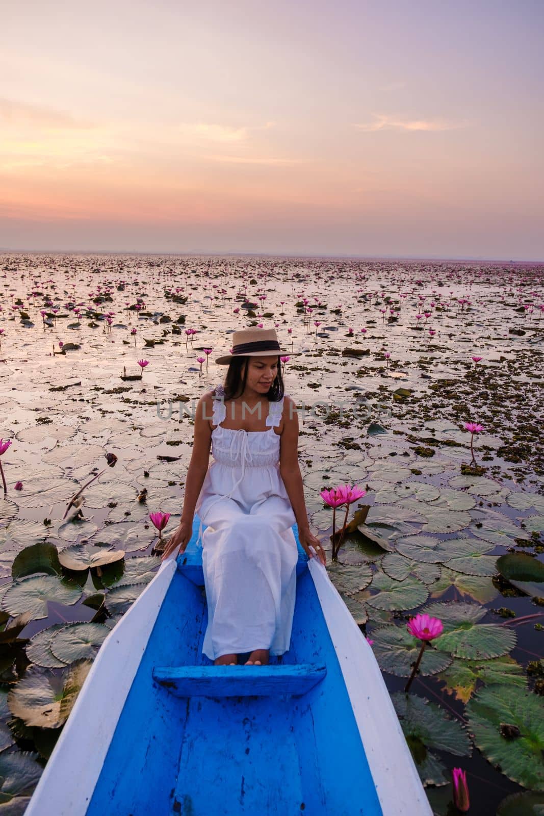 Asian women with a hat in a boat at the Red Lotus Sea full of pink flowers in Udon Thani Thailand. by fokkebok