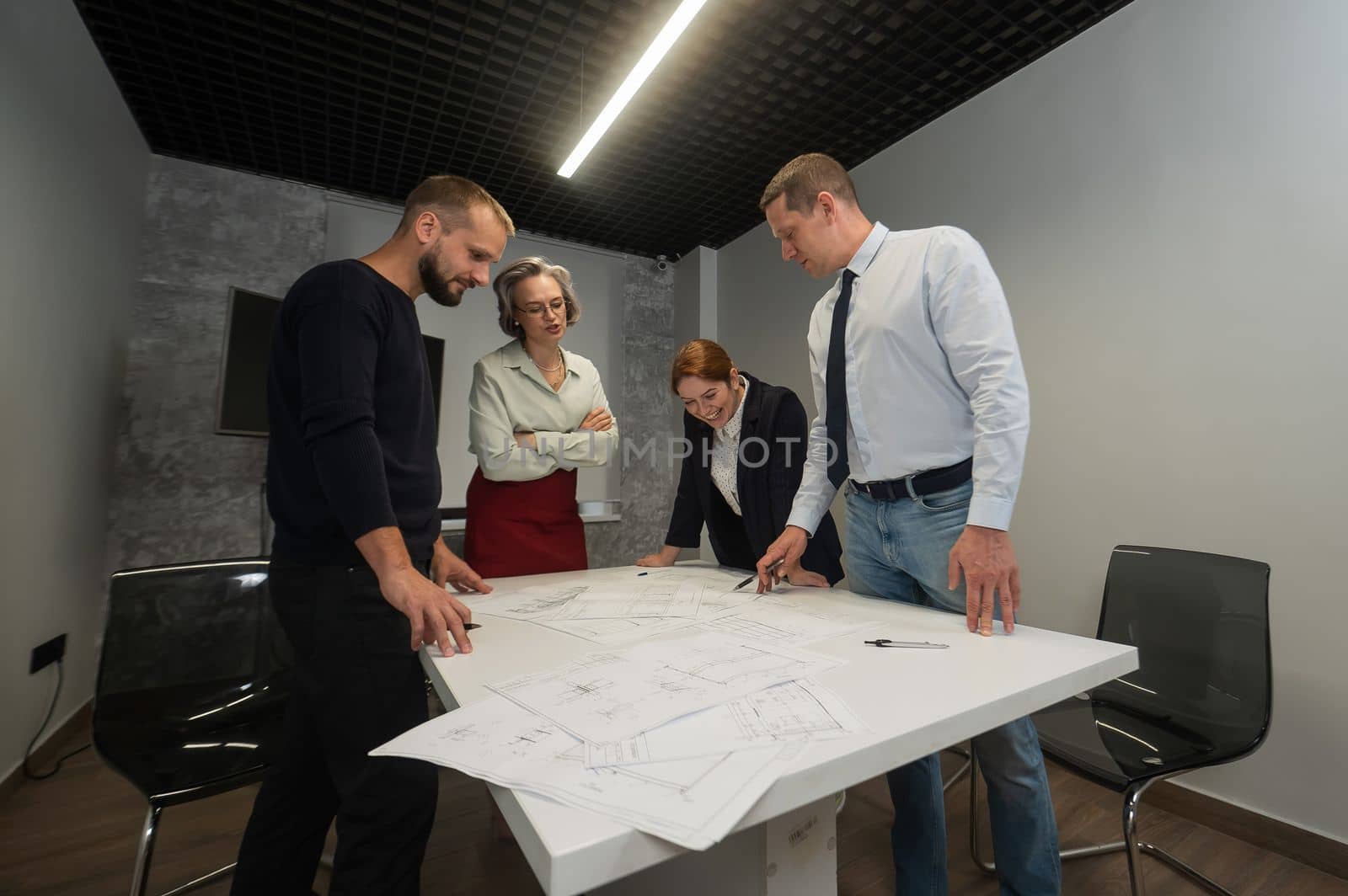 Four business people review and discuss blueprints. Designers engineers at a meeting