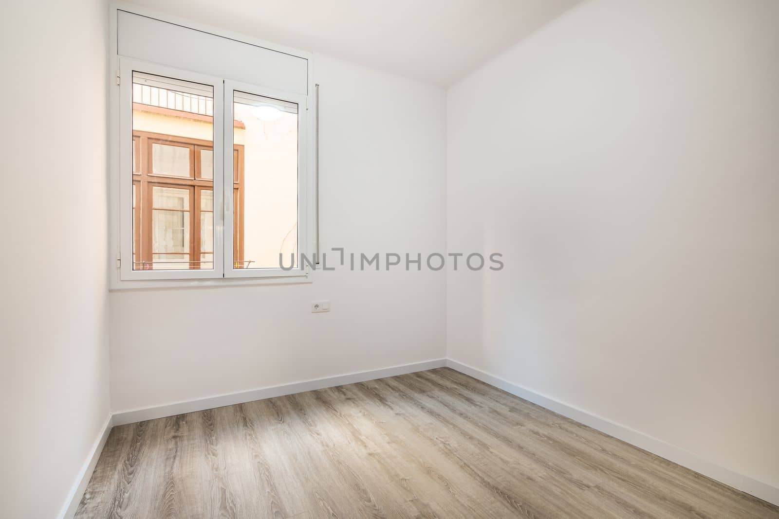 An empty bright room with a window in which the windows of a nearby house are visible. External metal shutters are built into the window to darken the room during daylight hours. by apavlin