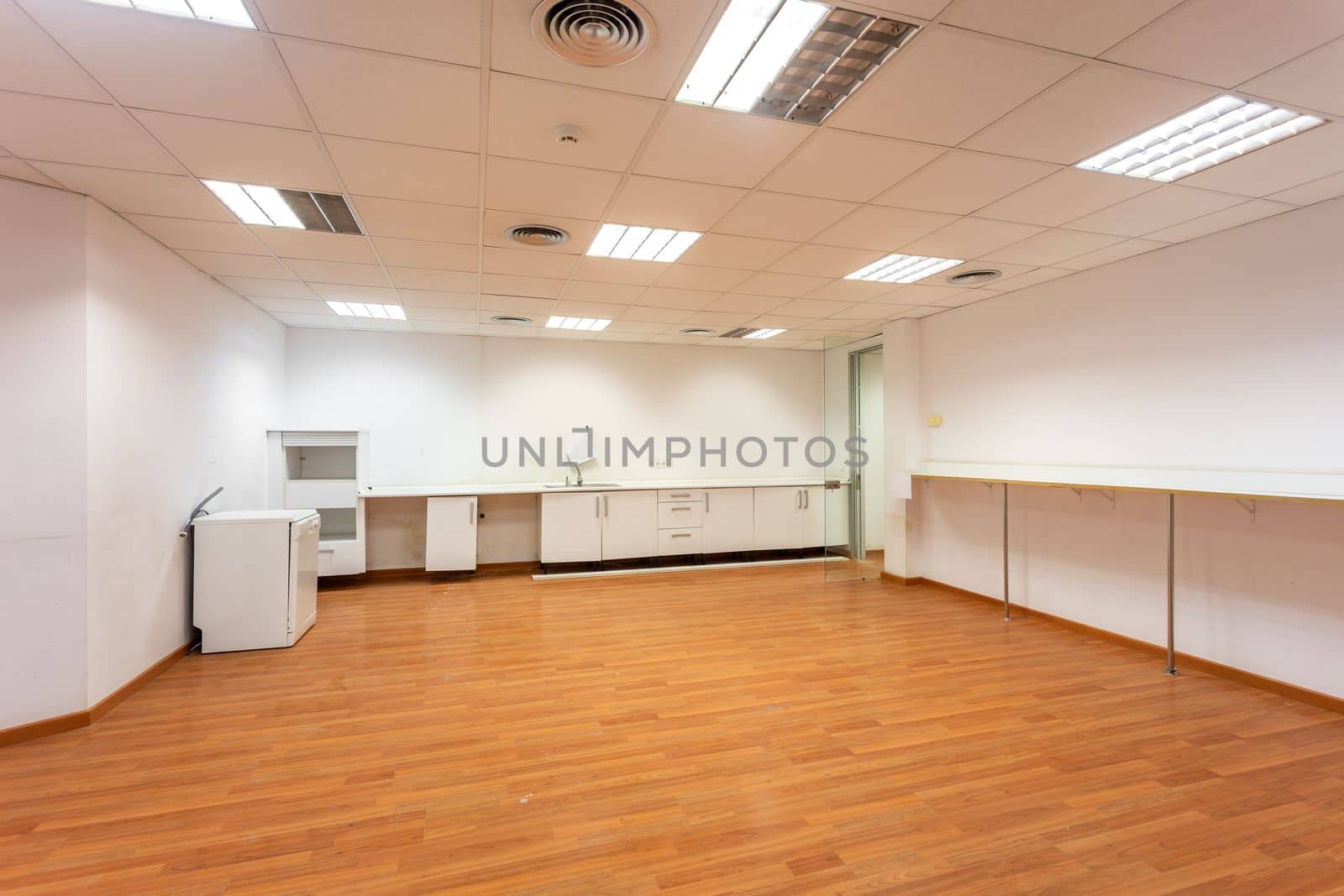 Old empty room with white kitchen furniture and sink that used to serve as office canteen for employees. A spacious and bright room, equipped as corporate dining room, needs new and fresh renovation