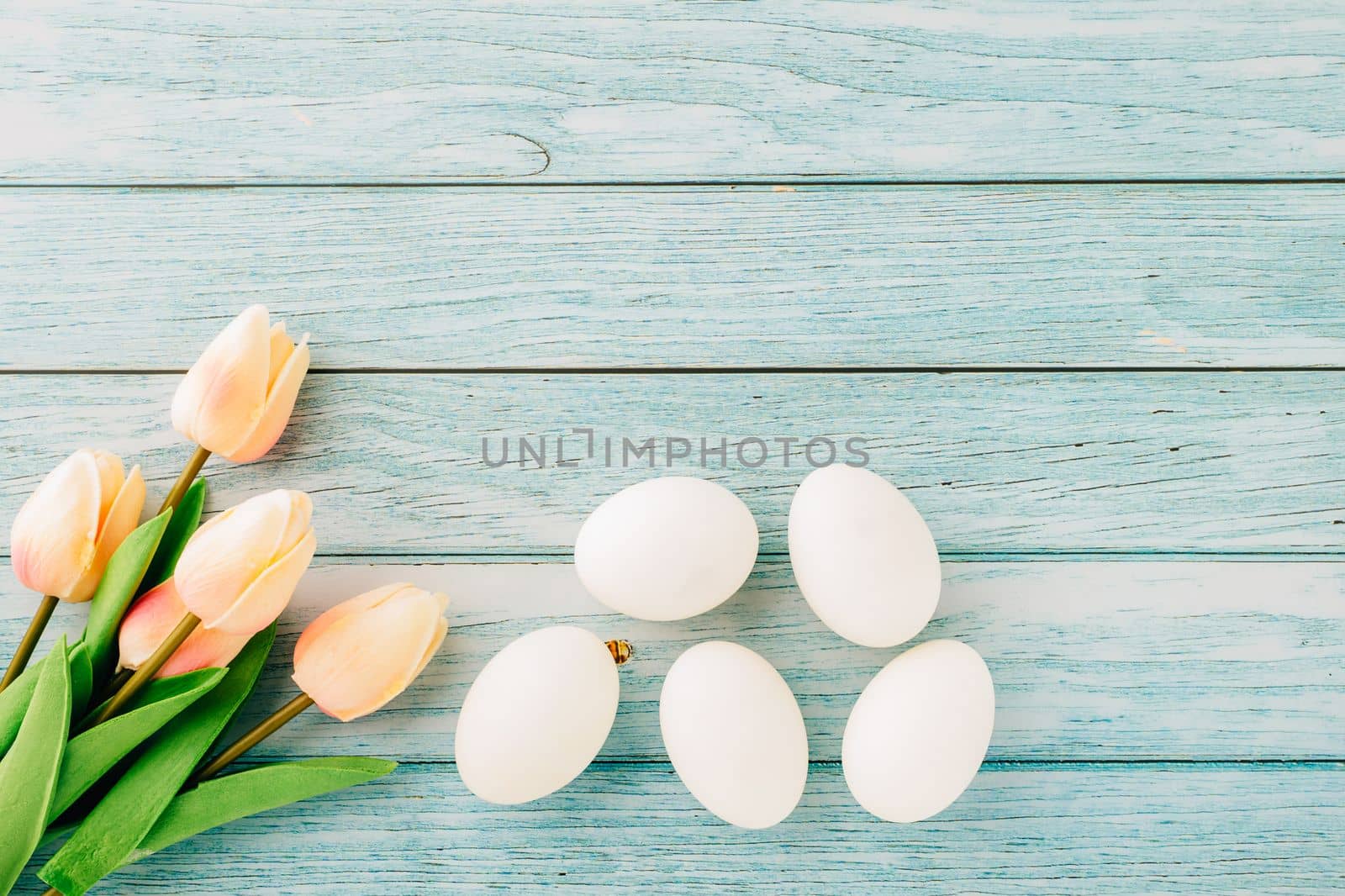 Happy Easter Day Concept. Top view of holiday banner background design white easter eggs and spring tulip flowers on blue wooden background with empty copy space, celebration greeting card