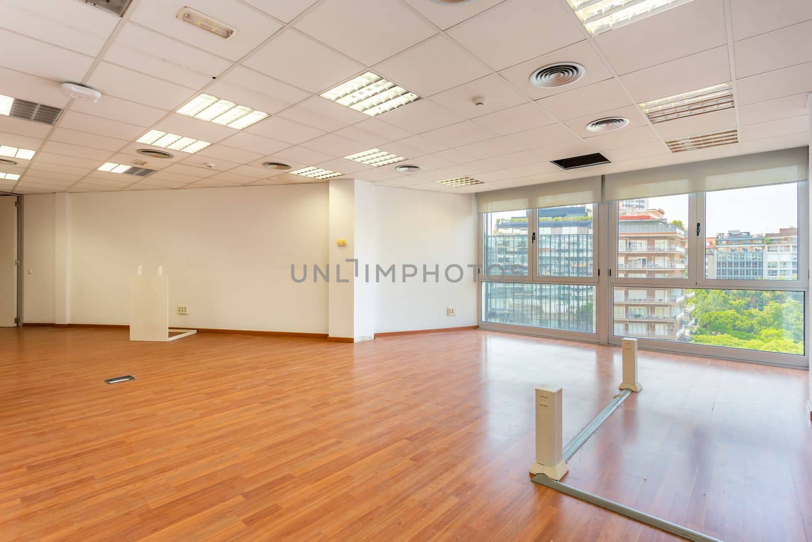 Empty office and fluorescent lamps on the ceiling in need of repair and replacement. Bright office space for rent. Light brown parquet and large panoramic windows in an empty abandoned office. by apavlin