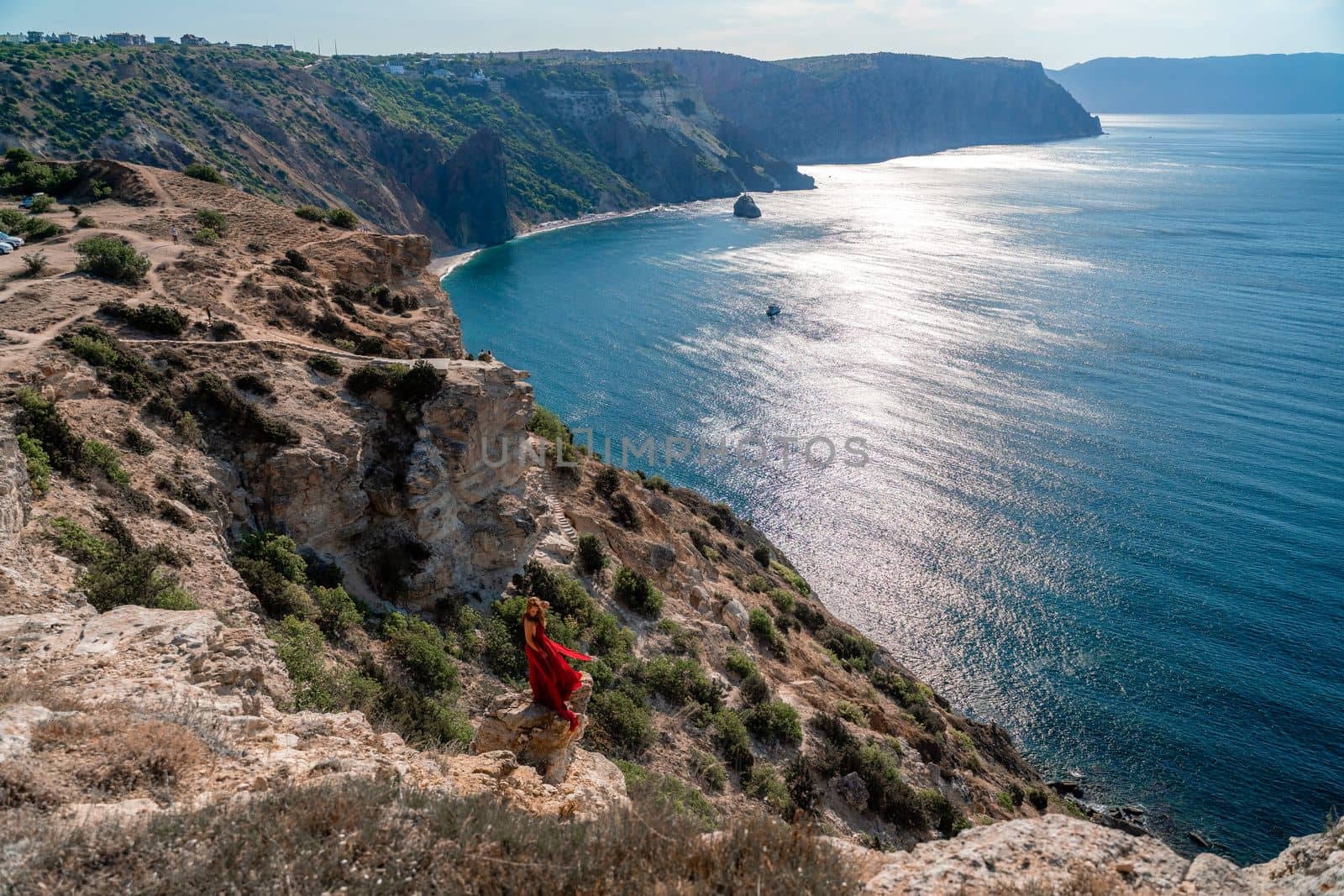 A woman in a red flying dress fluttering in the wind, against the backdrop of the sea