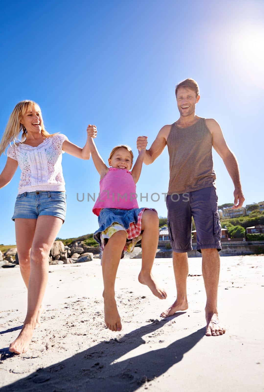 The beach is a great place for family bonding. a happy young family enjoying a walk on the beach. by YuriArcurs