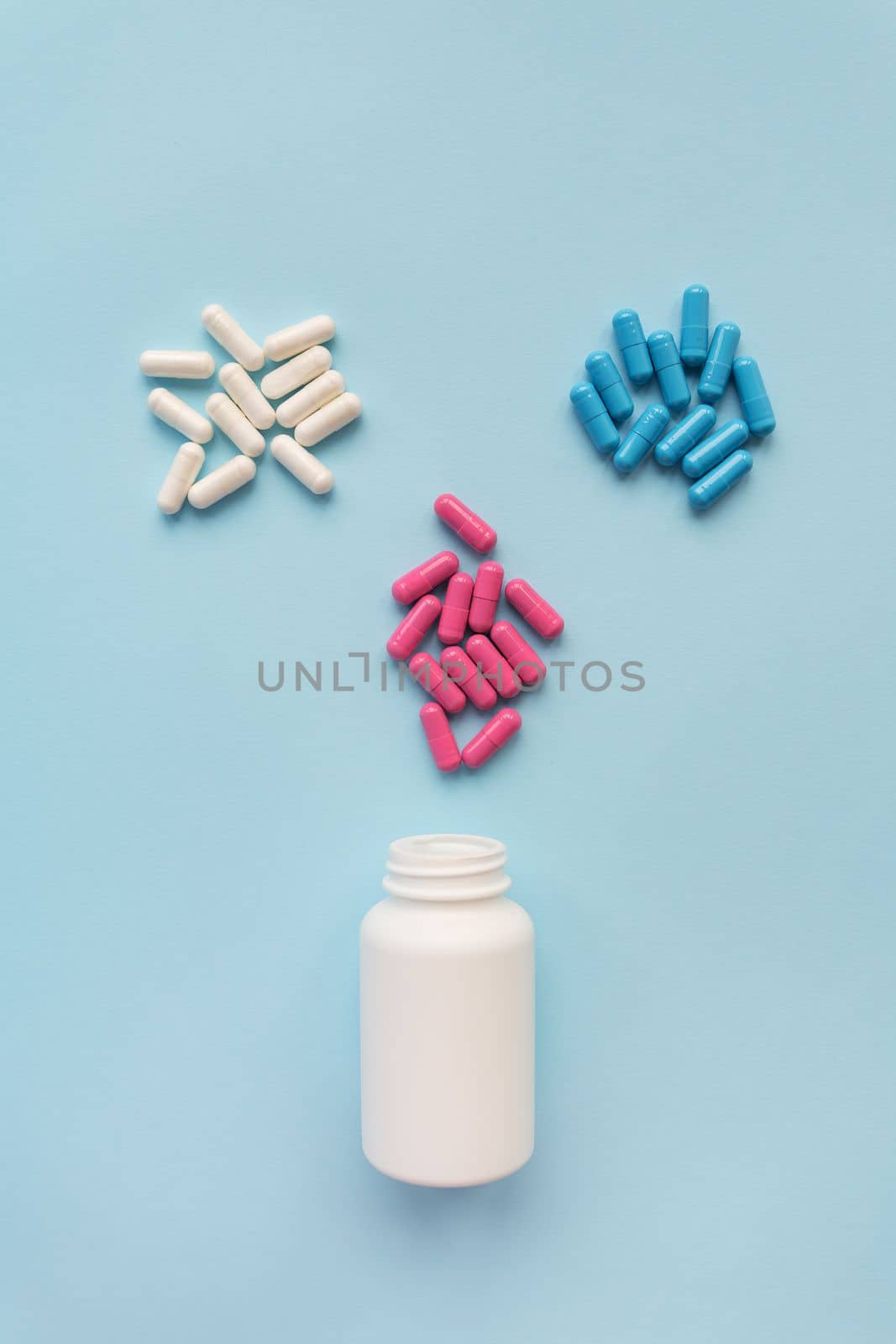 Various multicolored bright capsule pills flying from an open plastic bottle isolated on a blue background. The concept of evidence-based medicine and healthcare