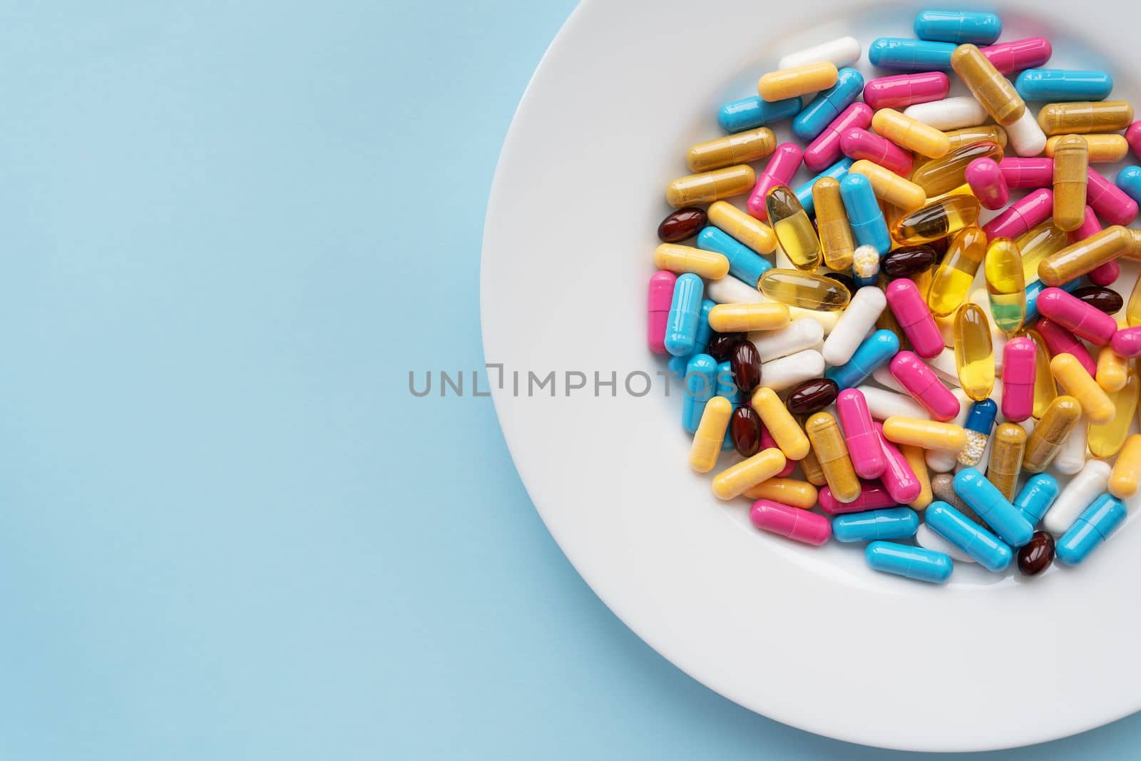 Colorful pills in a large white bowl on a blue background. The concept of health and evidence-based medicine