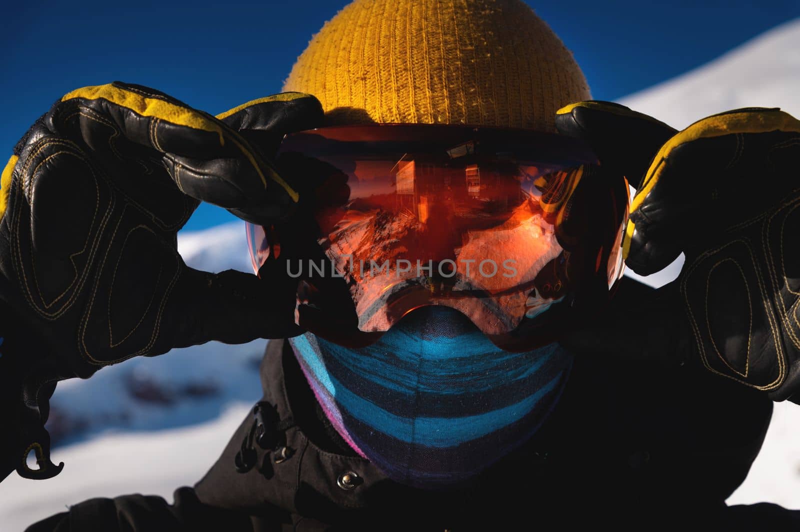 Skier in ski goggles with reflection of snow-capped mountains in them. Portrait of a man in a ski resort against the backdrop of mountains and blue sky.