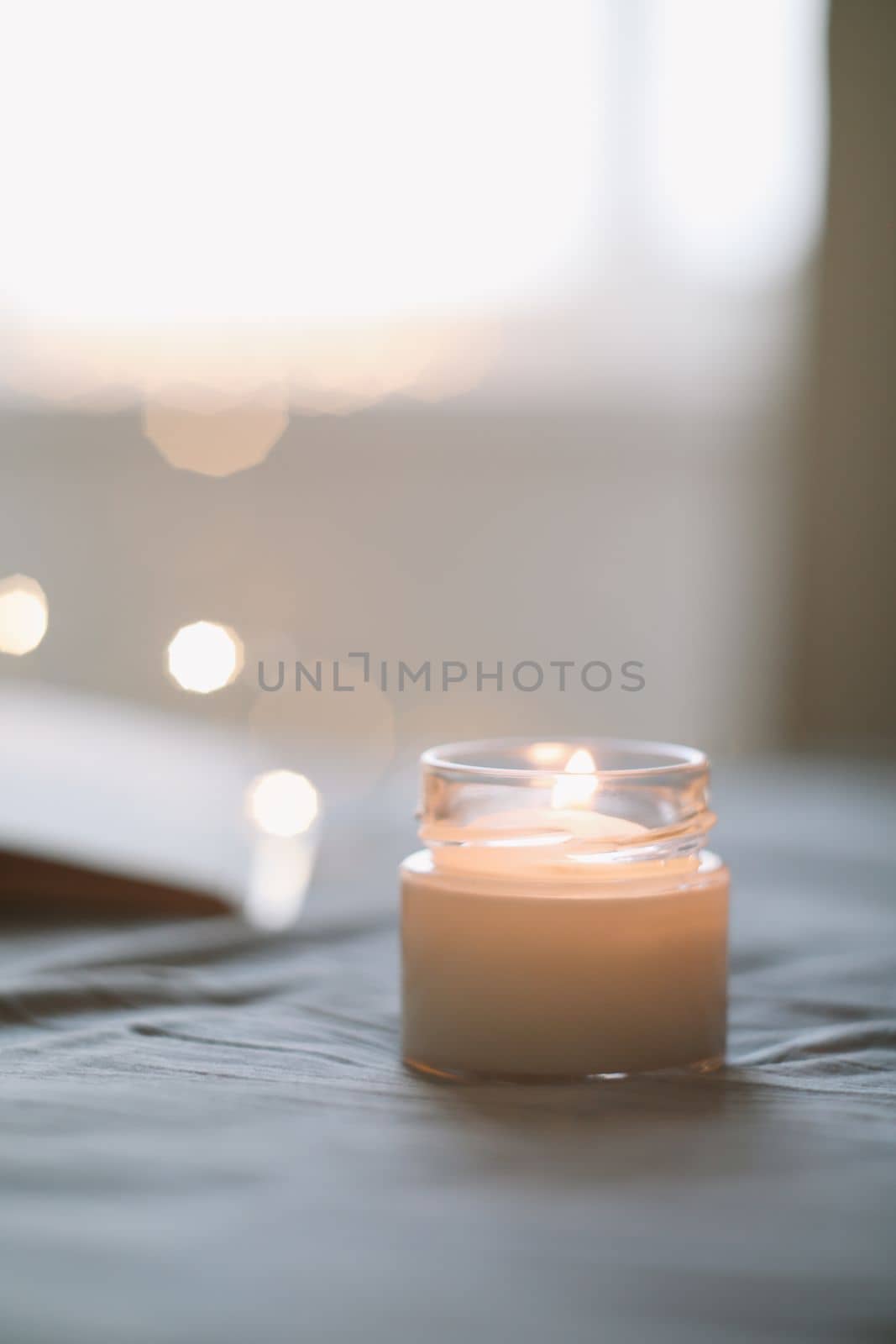 Burning candle in bed close up over lights. Cozy still life composition. home decor