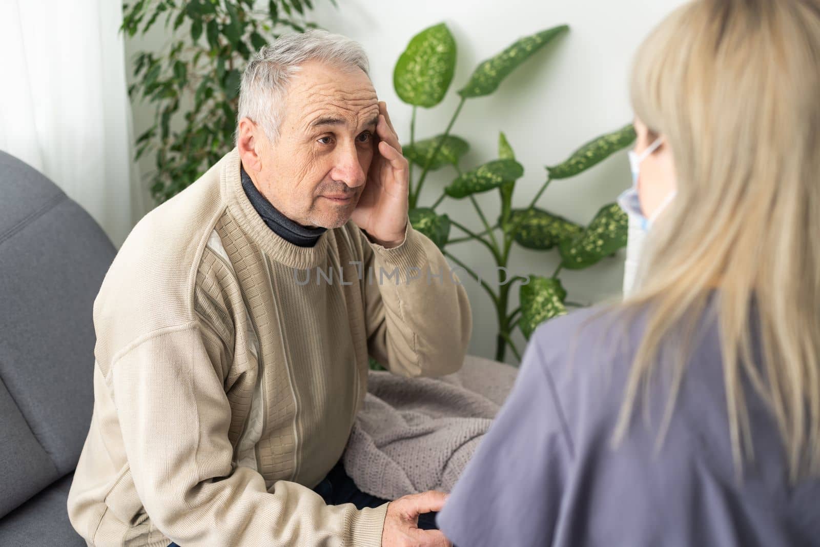 Caring nurse talks to old patient holds his hand sit in living room at homecare visit provide psychological support listen complains showing empathy encouraging. Geriatrics medicine caregiving concept.