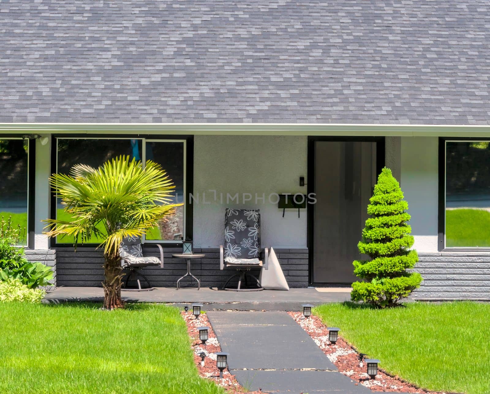 Main entrance of residential house with concrete pathway over the front yard on bright sunny day.