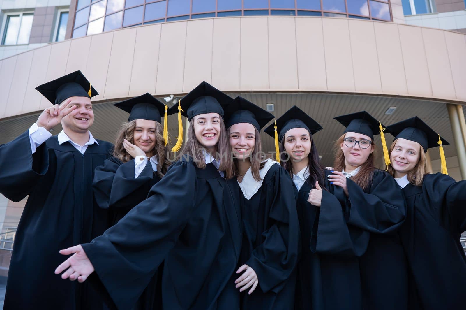 Happy students in graduate gown stand in a row against the backdrop of the university