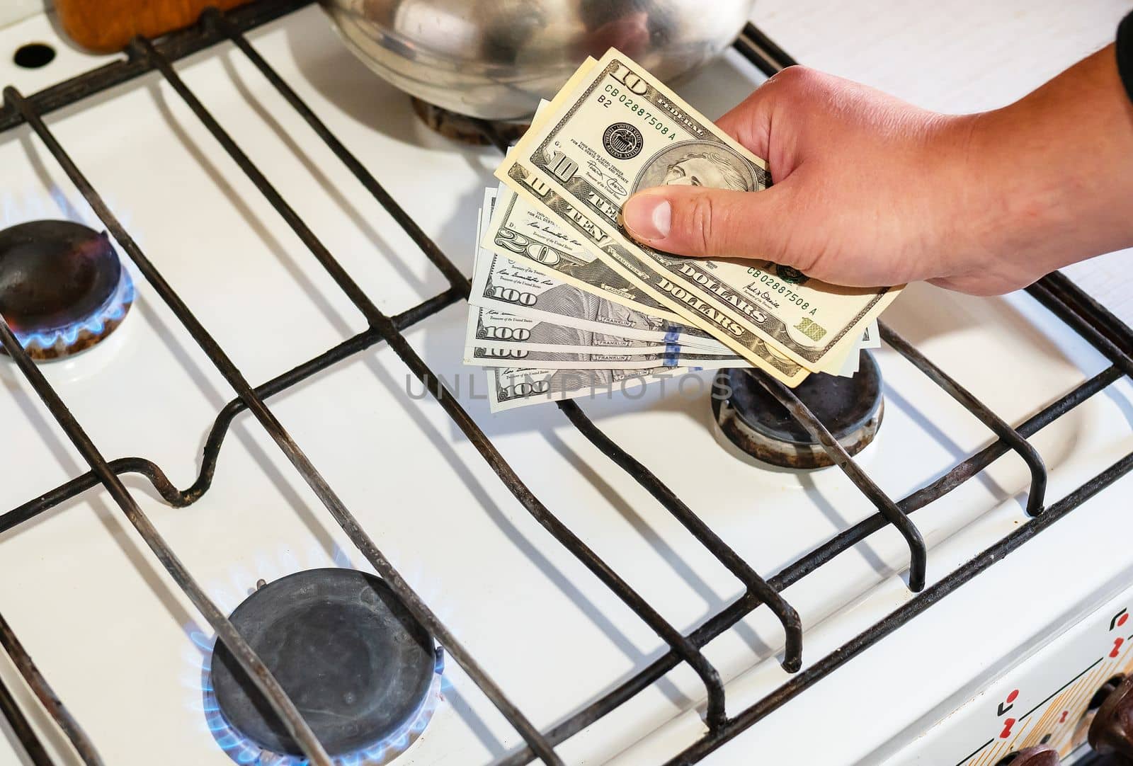 Payment of utility services. Dollar bills are held in their hands near a burning gas burner. The concept of increasing the cost of natural gas supply and payment