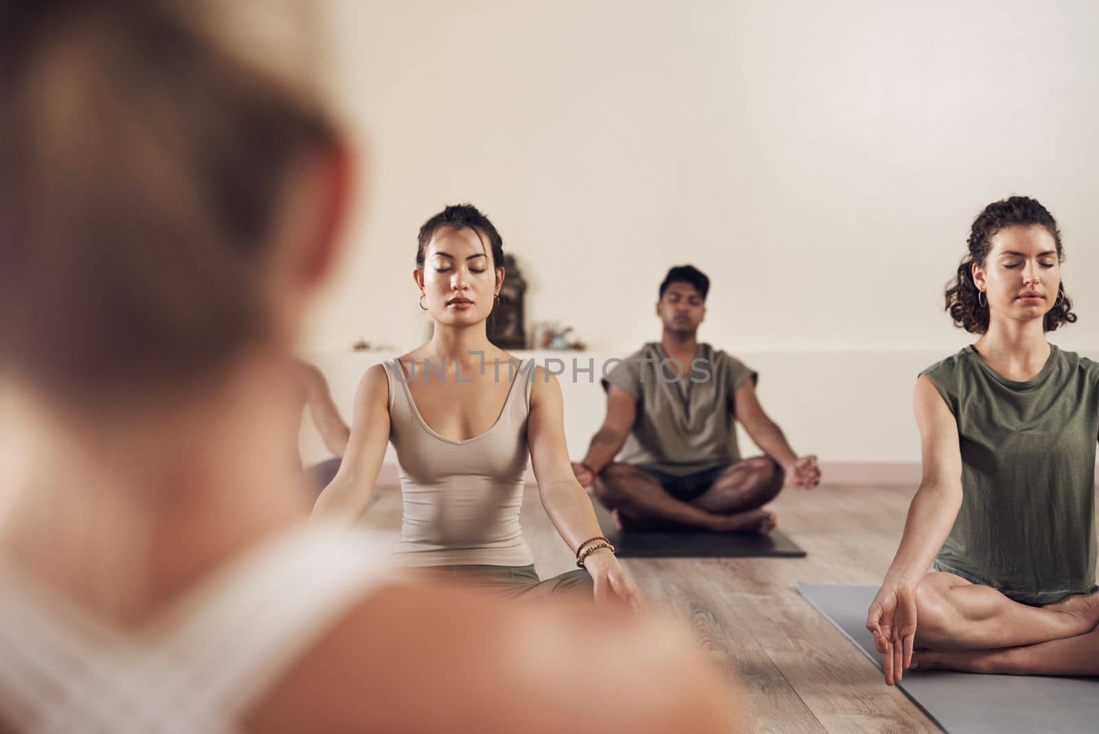 Healthy bodies stem from healthy minds. a group of young people meditating and practicing yoga together inside a yoga studio. by YuriArcurs