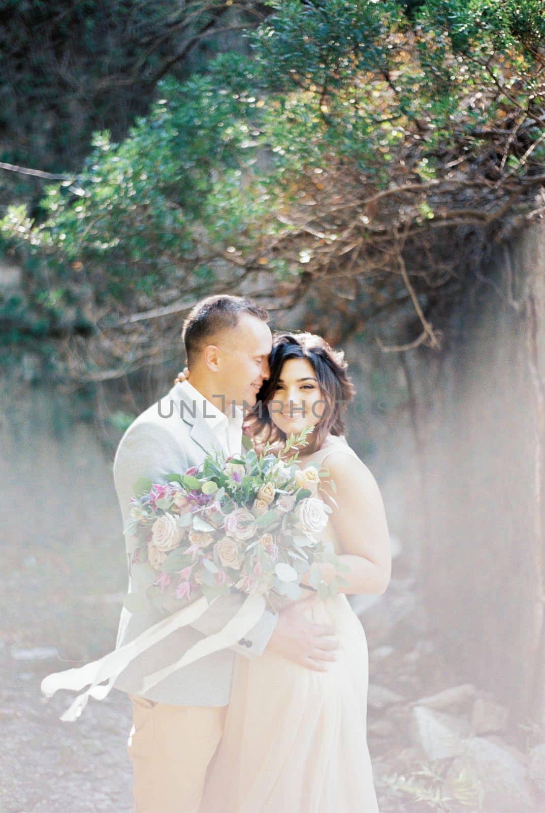 Groom hugs smiling bride with a bouquet in the garden. High quality photo