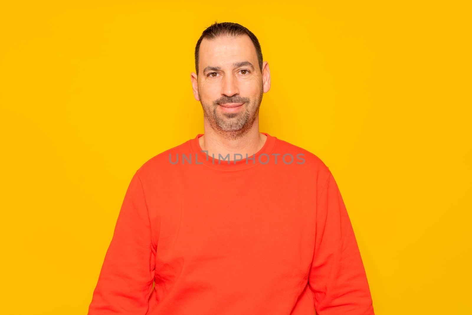 Isolated photo of a handsome man with a beard, wears a casual red sweater. He has a cheerful and relaxed expression, he is happy and content with his life.