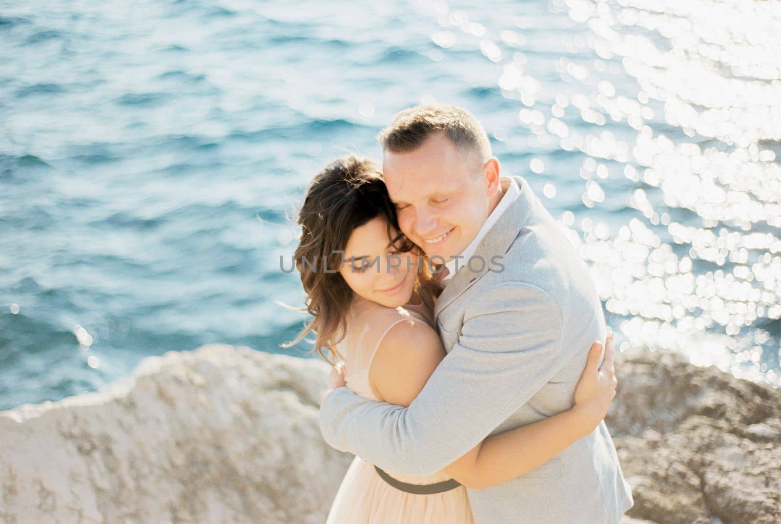 Groom hugs bride standing on a rock above the sea. High quality photo
