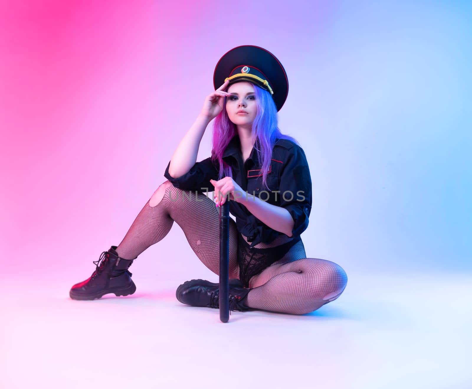 Sexy girl in police uniform posing in underwear with a police rubber baton in neon light on an empty background