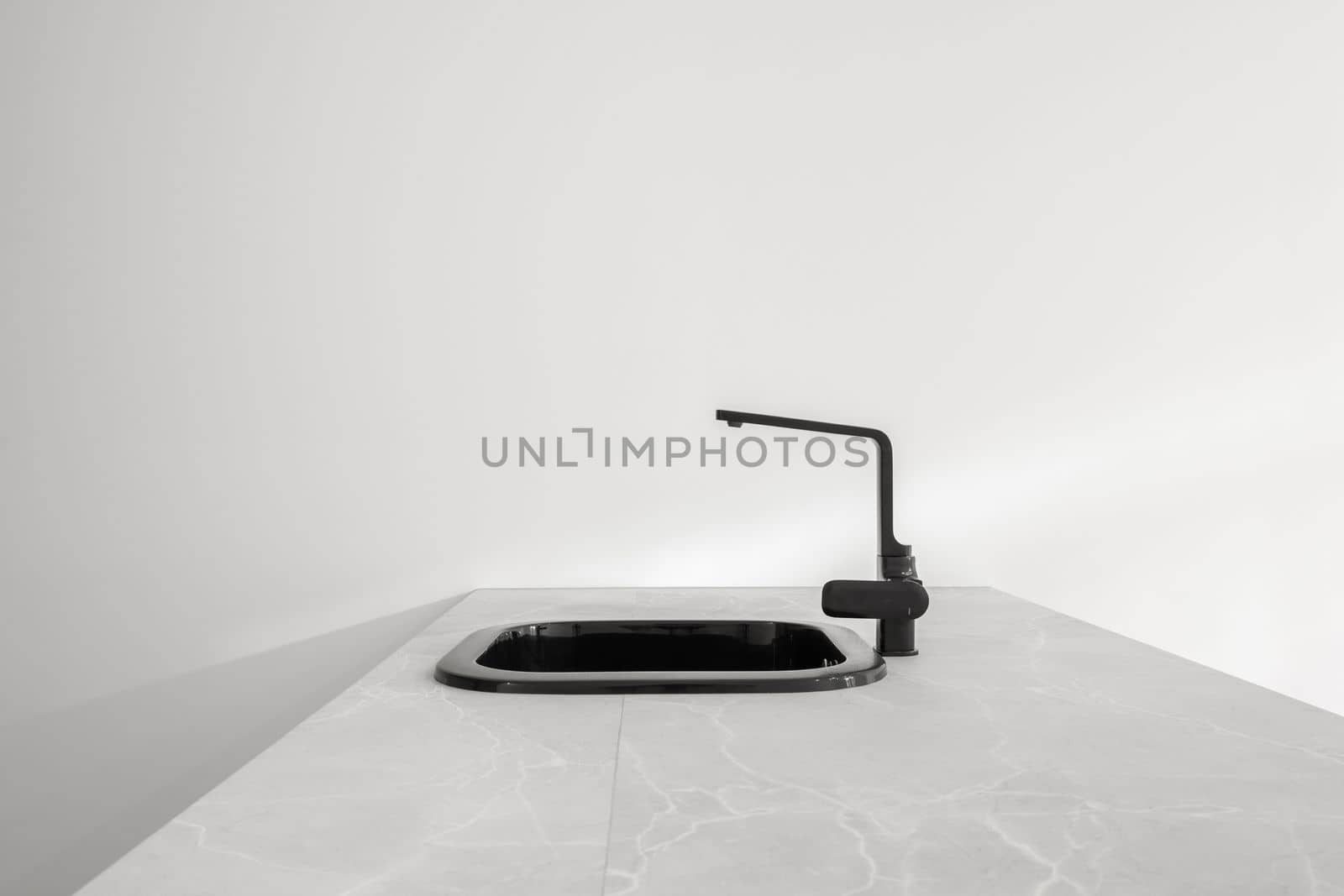 Black metal kitchen sink with trendy faucet sits on large white stone kitchen island on light background. Concept of kitchen after renovation or in new building. New plumbing by apavlin