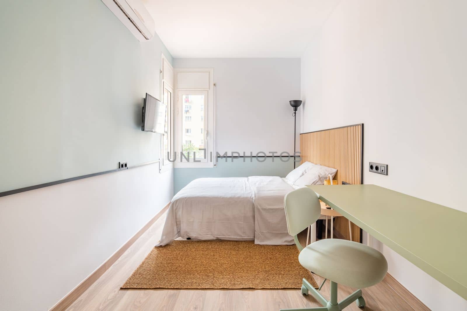 Narrow long room with bed, on opposite wall is TV for viewing watchable content. In corner is floor lamp with black shade for soft lighting at night. On floor is soft warm brown carpet. by apavlin