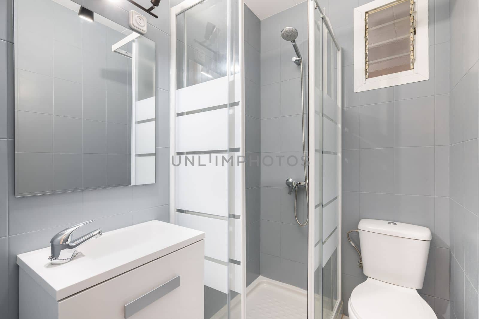 Compact modern bathroom in gray and white tones with shower with glass doors, toilet bowl and sink with cabinet for storing things. Concept of a toilet design idea in a compact apartment by apavlin