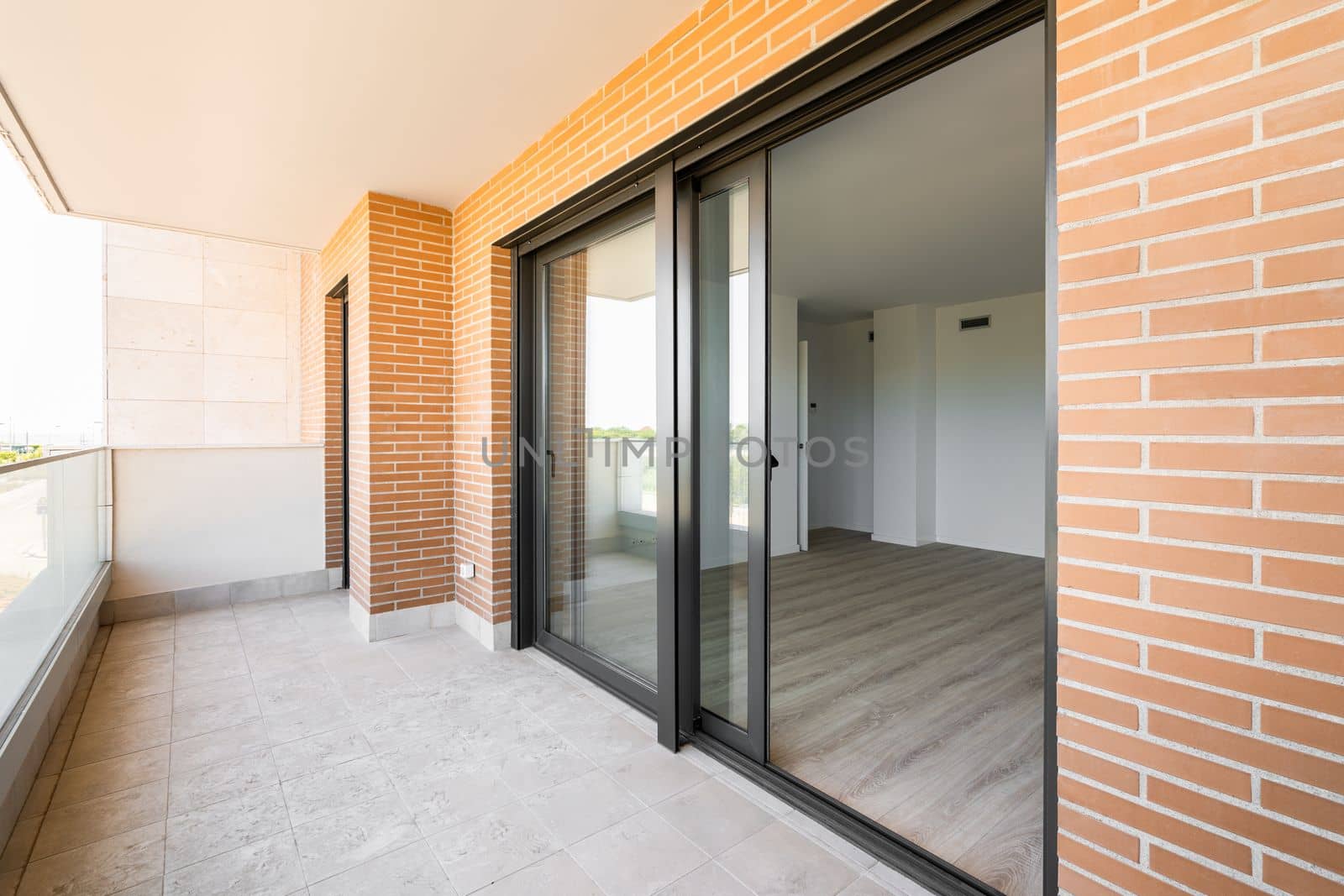 Side view of terrace opening after the large panoramic windows in luxury apartment of new building made of red brick and black metal frames. Concept of open air zone in the house.