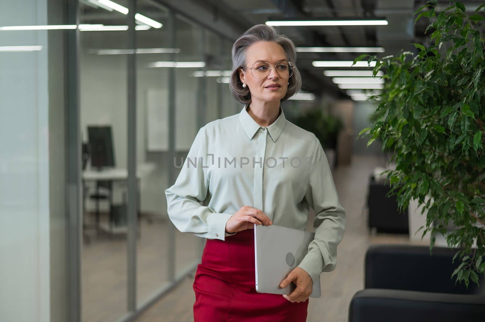 Mature caucasian woman stands with a laptop among the office