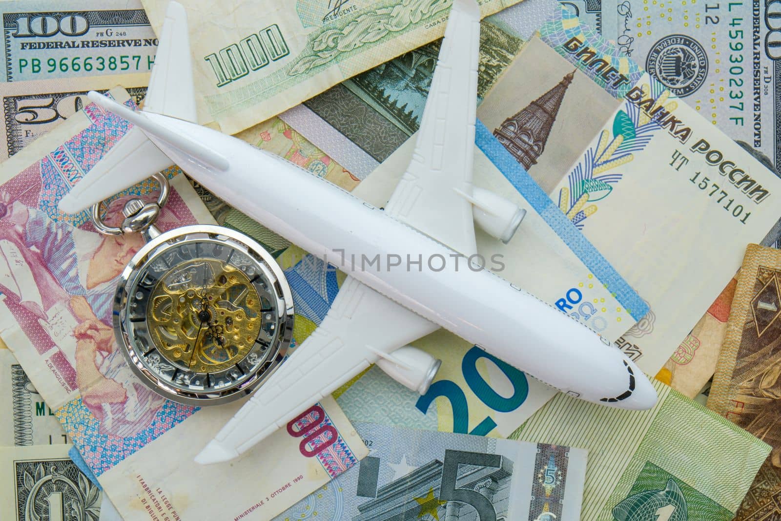 Pocket watch, airplane sitting on arrangement of international currencies including euro, ruble USD. Concept of high cost of travel. High quality photo