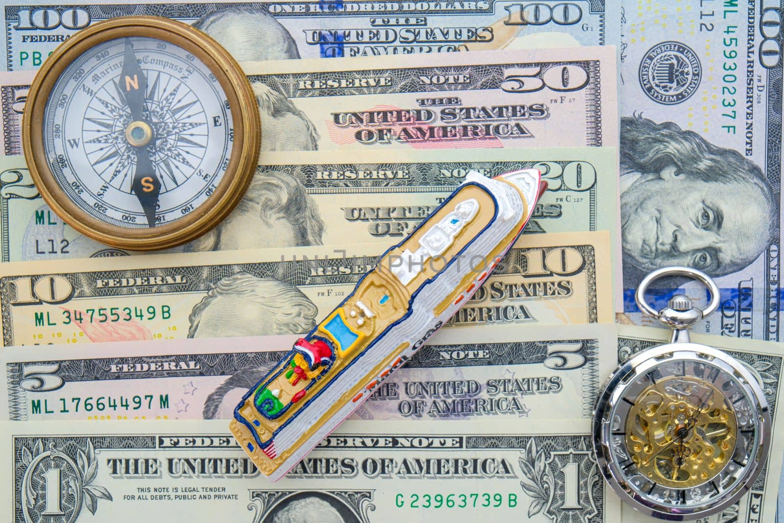 Time and travel cost concept. Miniature cruise ship, watch, compass on layout of US currency, denominations one to 100. High quality photo