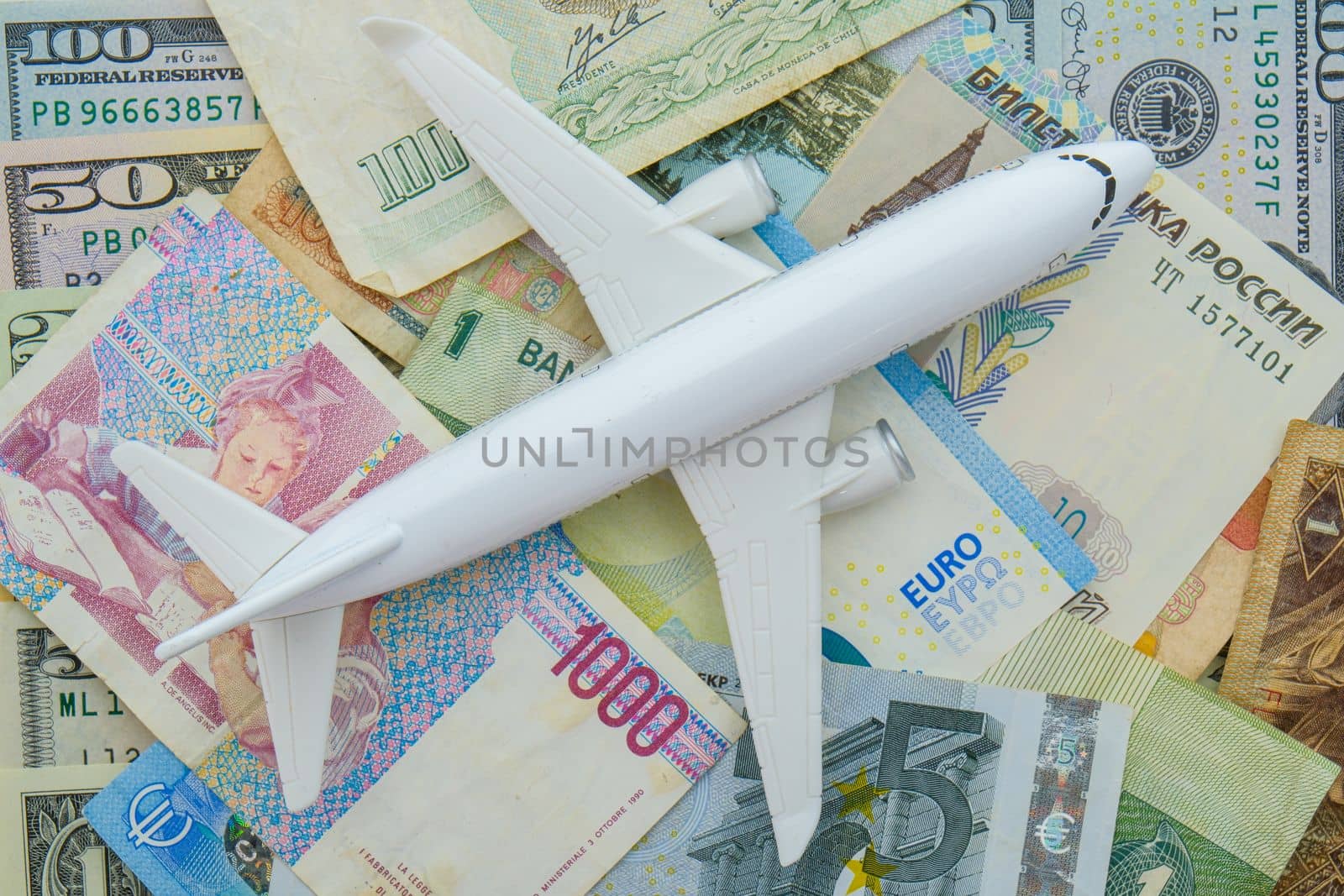 Passenger plane sitting on world currency bills including ruble, euro, USD, showing concept high cost of flying, travel. High quality photo