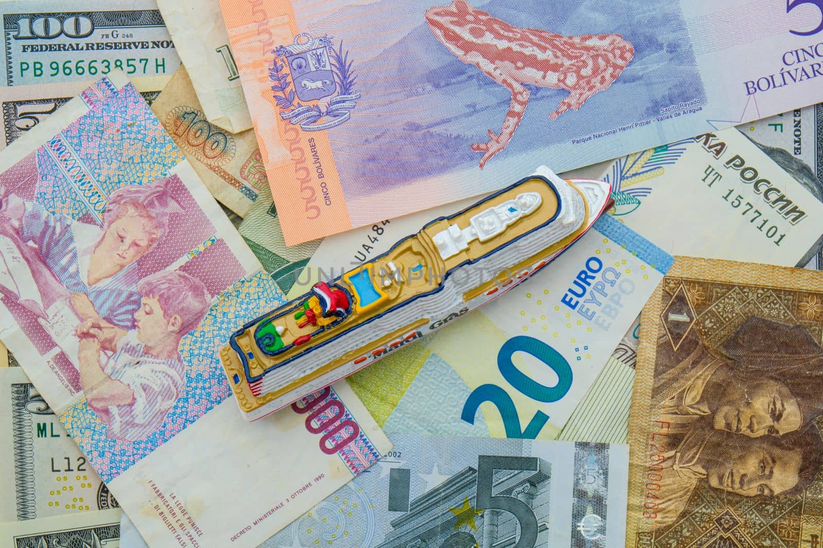 A miniature cruise ship on a background of international currencies including ruble, euro, USD top down view. High quality photo