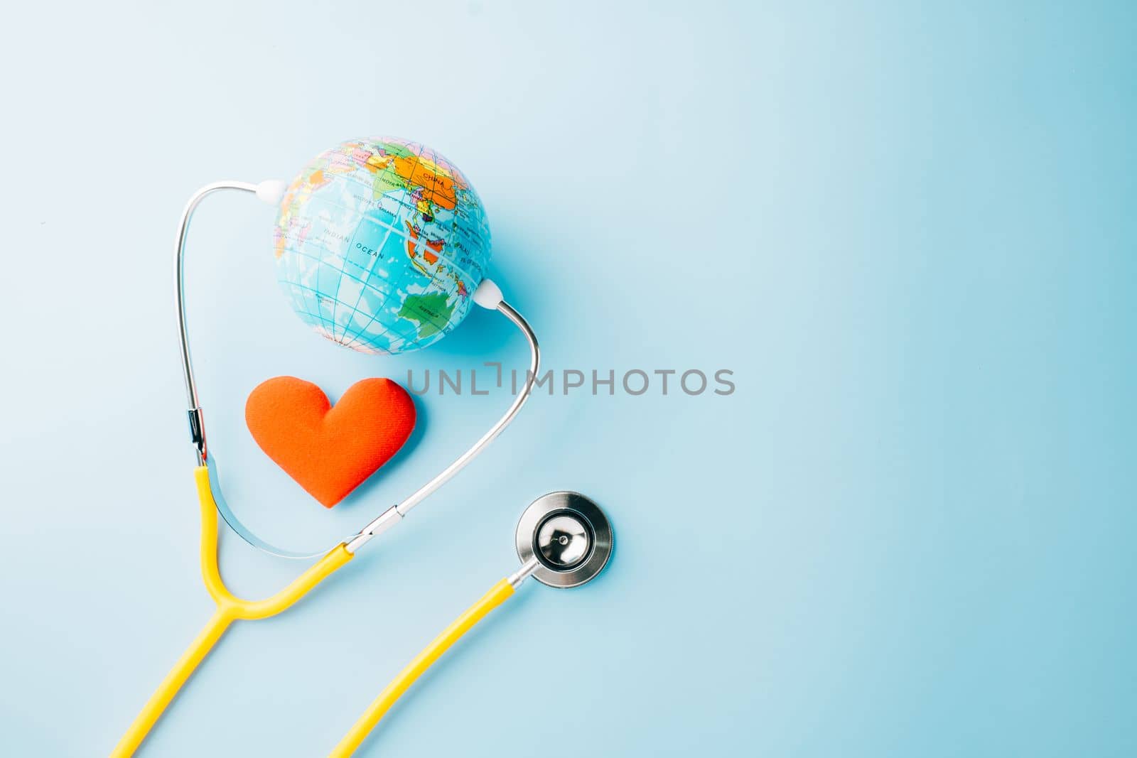 World Health Day. Yellow doctor stethoscope and world globe with Red heart shape isolated on blue background with copy space, Save world day, Green Earth Environment, Healthcare and medical concept