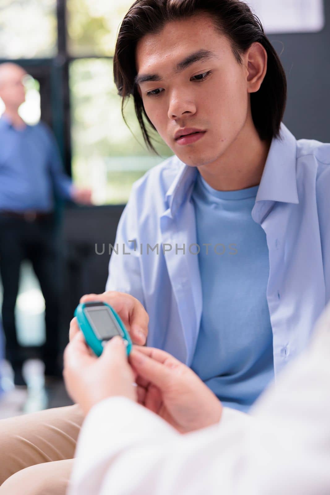 Elderly physician measuring insulin and glucose level with glucometer while doing health examination with diabetic asian patient. Using insturment to check blood sample in hospital waiting area