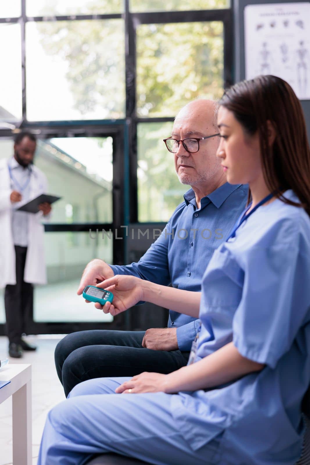 Asian physician nurse examining elderly patient with glucometer during consultation, measuring insulin and glucose level from blood sample. Old man doing diabetic control in hospital waiting area