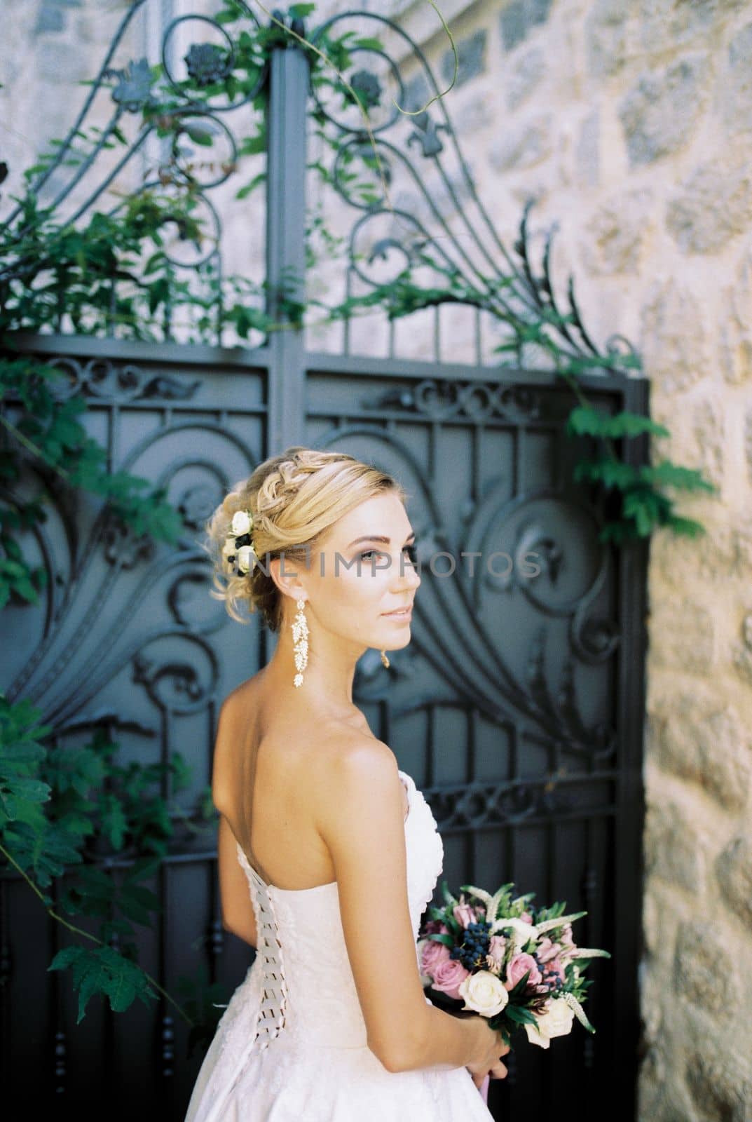 Bride with a bouquet stands sideways near a stone house. High quality photo