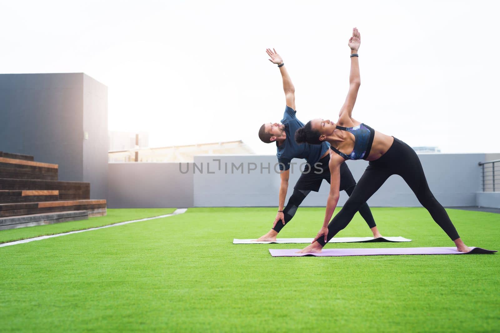 Yoga helps in retaining the vitality in your body and mind. a young man and woman practising yoga together outdoors. by YuriArcurs