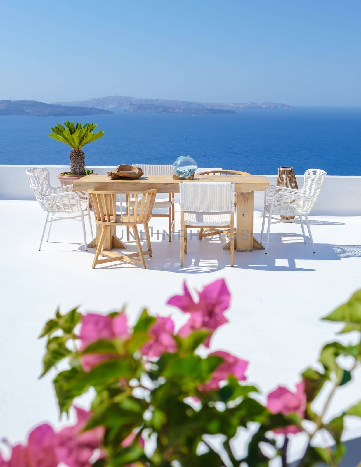 outside terrace of a restaurant by the ocean of Santorini Greece, chairs, and tables with flowers by the ocean. 
