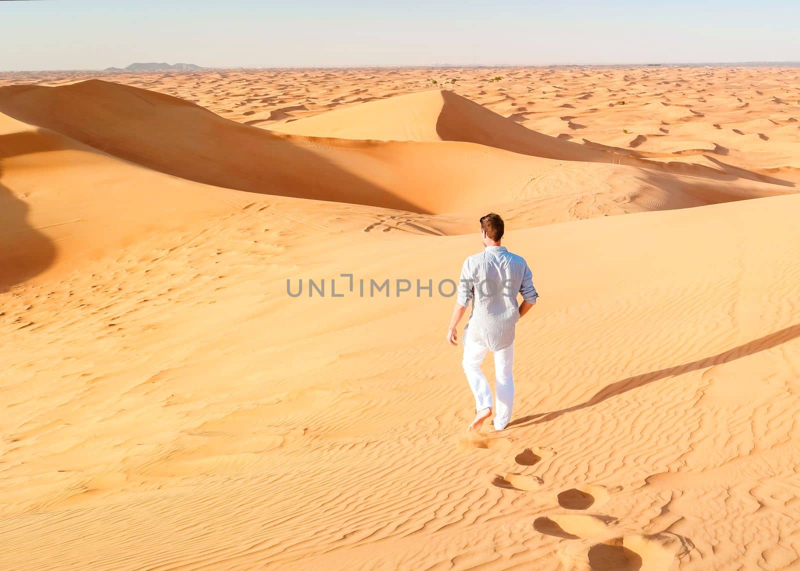 Young men walking in the desert of Dubai, Sand dunes of Dubai United Arab Emirates, sand desert on a sunny day in Dubai.