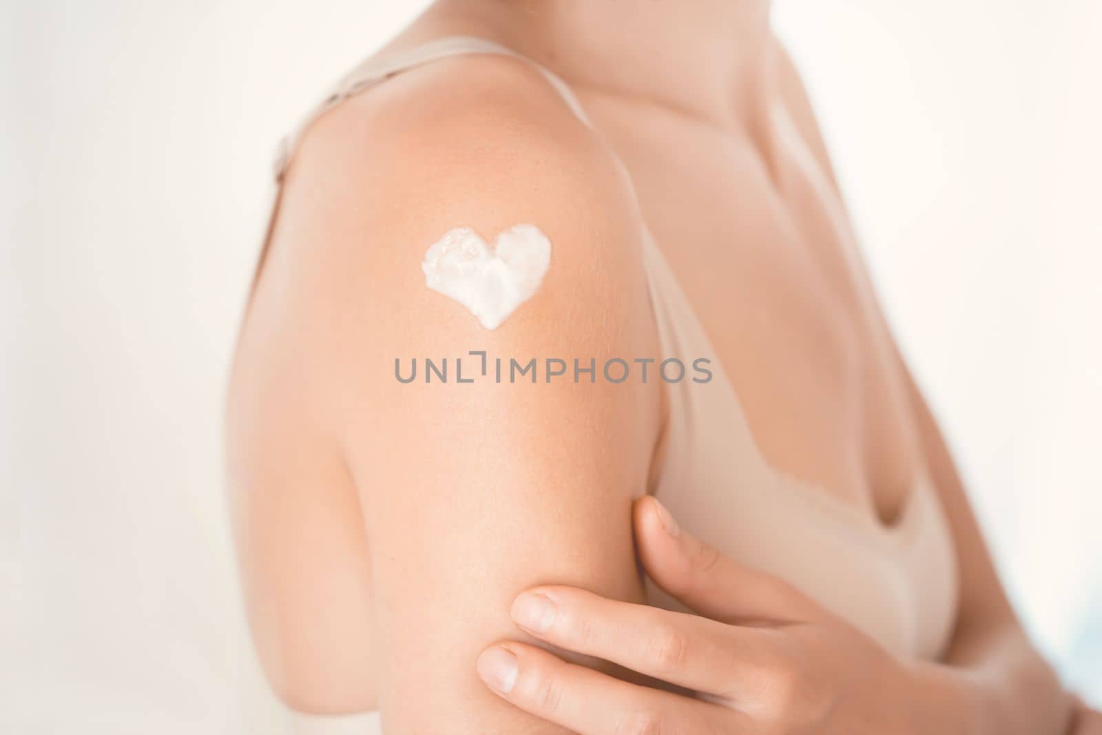 A young girl applies a moisturizer to her skin, a woman gently cares for her body, depicts a heart with a cream, taking care of herself, beauty and health.