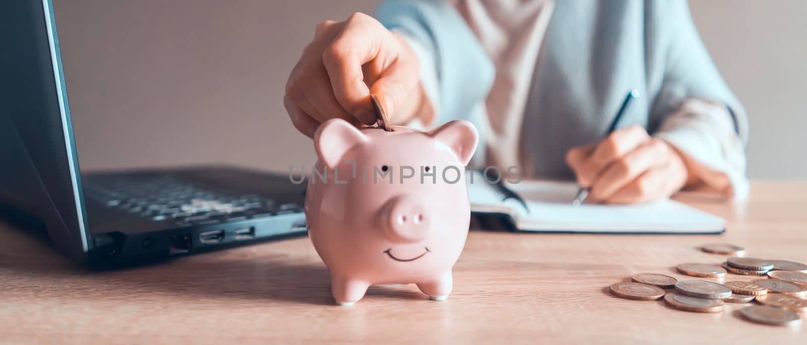 A young girl works at a laptop, writes a business development plan in a notebook, develops a strategy and makes calculations of earned funds. A woman puts her savings in a piggy bank.