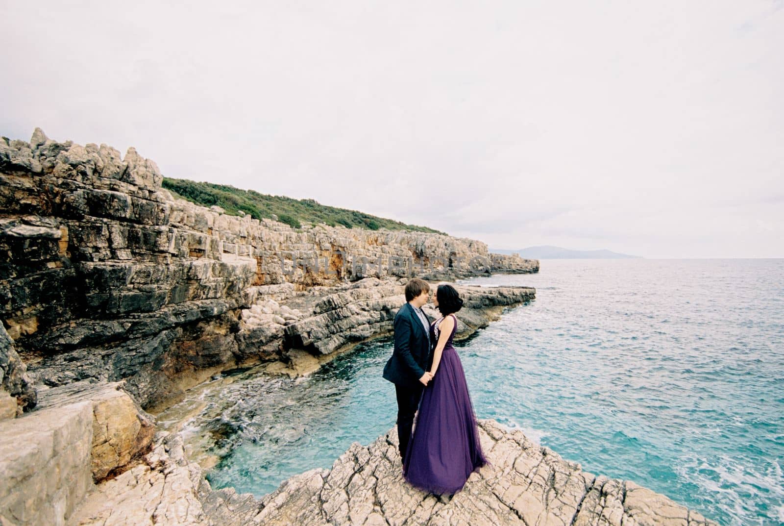 Man and woman stand hugging on a rock above the sea. High quality photo